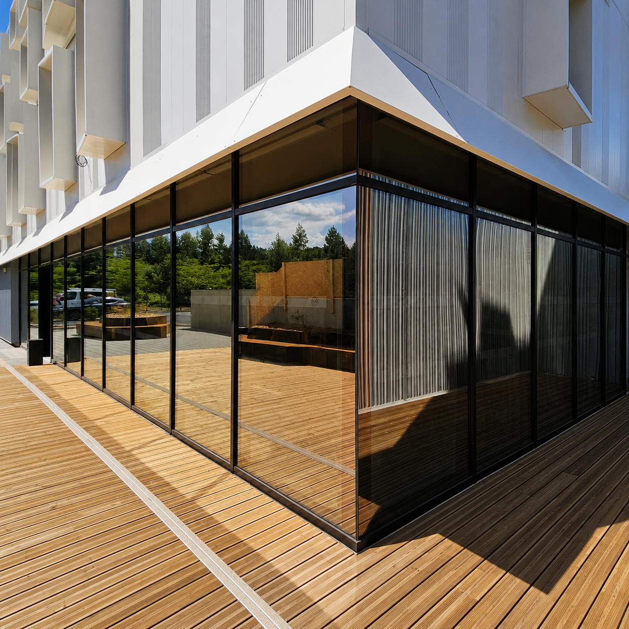 Façade vitrée en aluminium à l’angle d’un bâtiment, avec terrasse en bois