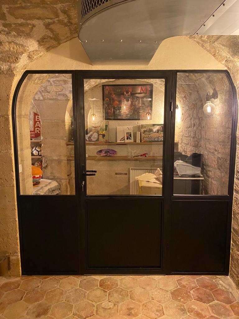 Cloison intérieure vitrée en acier, avec porte, dans une salle voûtée en pierre
